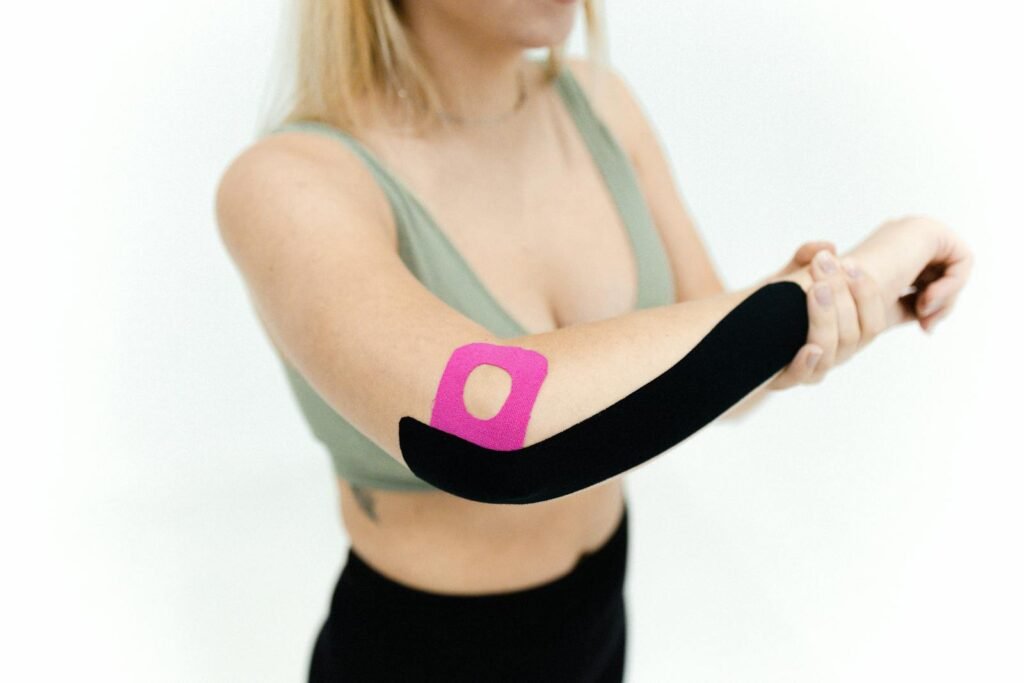 Roundups Hub 14 Injury prevention : Close-up of a woman applying kinesio tape on her arm for therapeutic treatment on a white background.